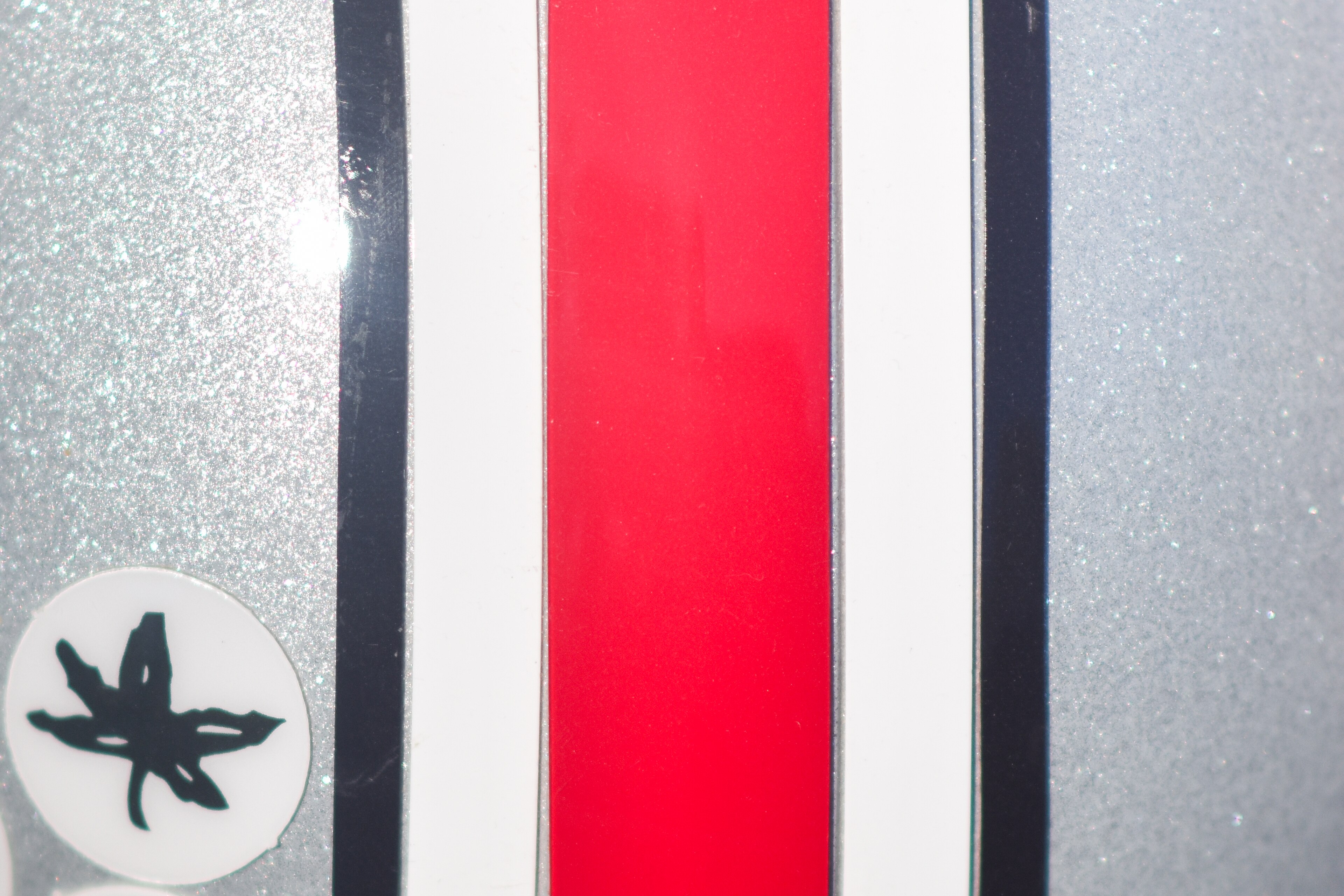 Close-up detail of an Ohio State football helmet's red, white, and black stripe beside a Buckeye leaf sticker.